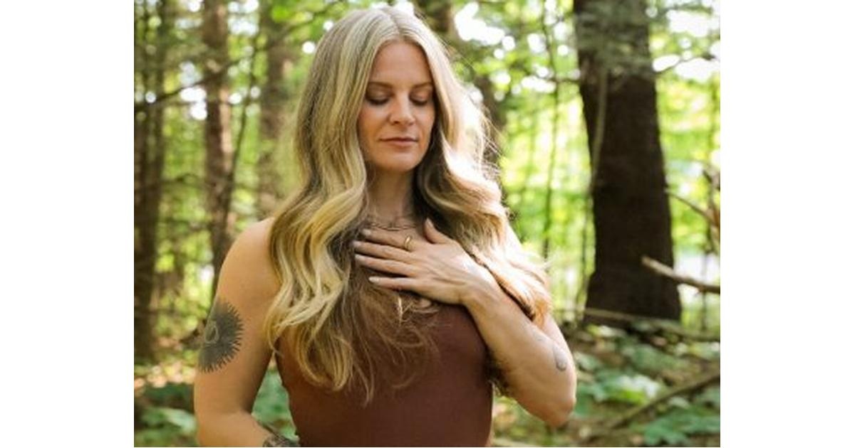 Energy clearing practitioner with hand over heart in peaceful forest setting.