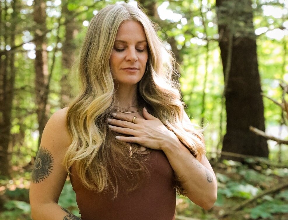 Energy clearing practitioner with hand over heart in peaceful forest setting.